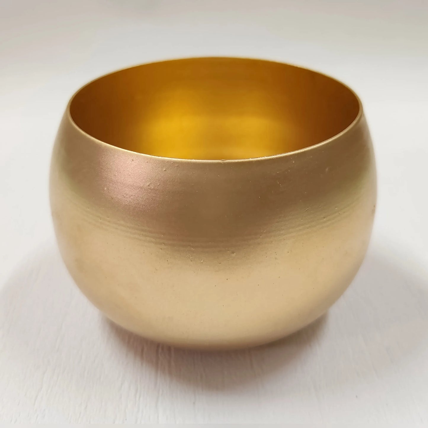 Gold ball candle tin held in hand with green plants in background