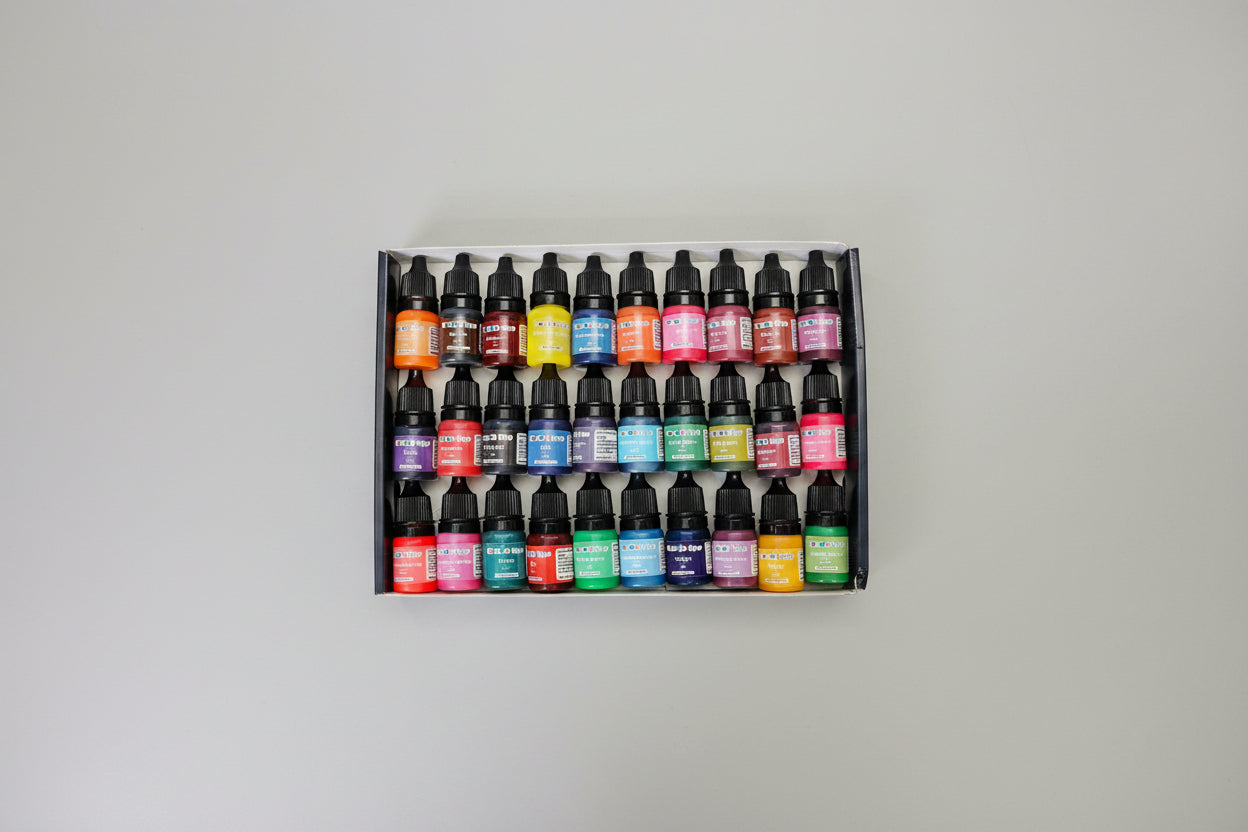 Set of ink bottles in various colors arranged in a box on a dark surface.