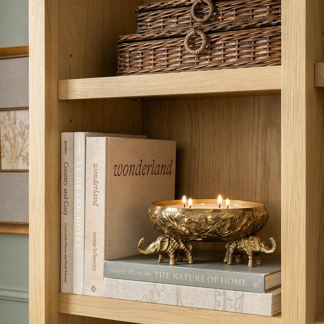 Gold elephant urli candle vessel with lit multi-wick candle on black dresser with stacked books