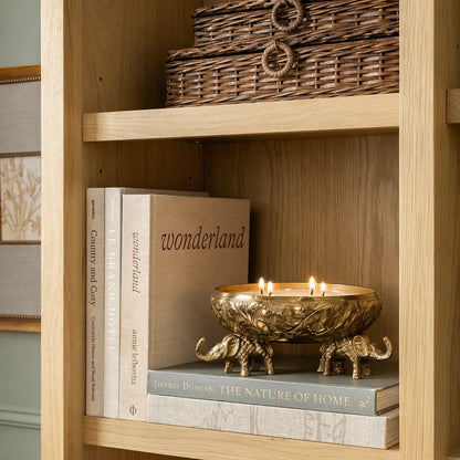 Gold elephant urli candle vessel with lit multi-wick candle on black dresser with stacked books