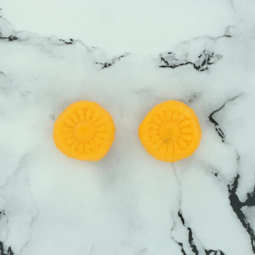 Two saffron orange peda shaped candles with embossed daisy pattern, top view on marble surface