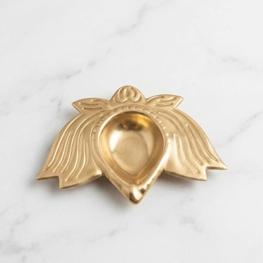 Gold metal lotus-shaped diya on white marble surface, top view showing petal wings and teardrop oil cup