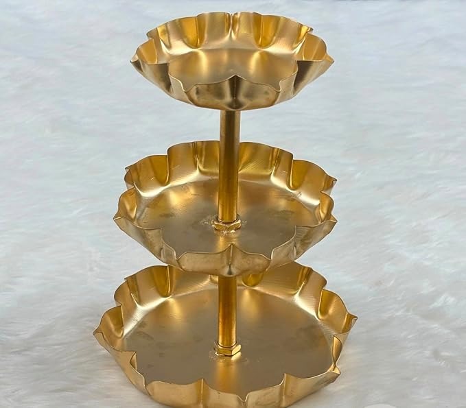 3-tier gold lotus petal tray stand on white surface with marigold flowers and diya in background