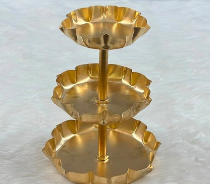 3-tier gold lotus petal tray stand on white surface with marigold flowers and diya in background