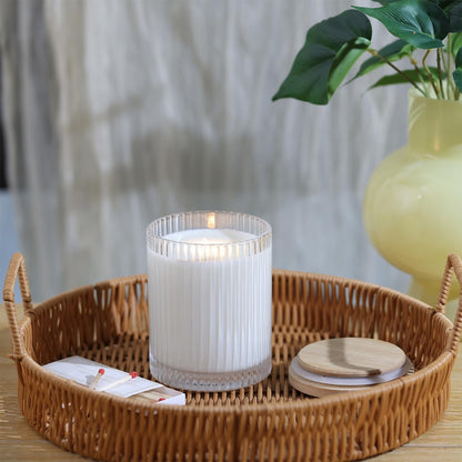 Single ribbed glass candle jar with lit candle on rattan tray with bamboo lid and matchbox