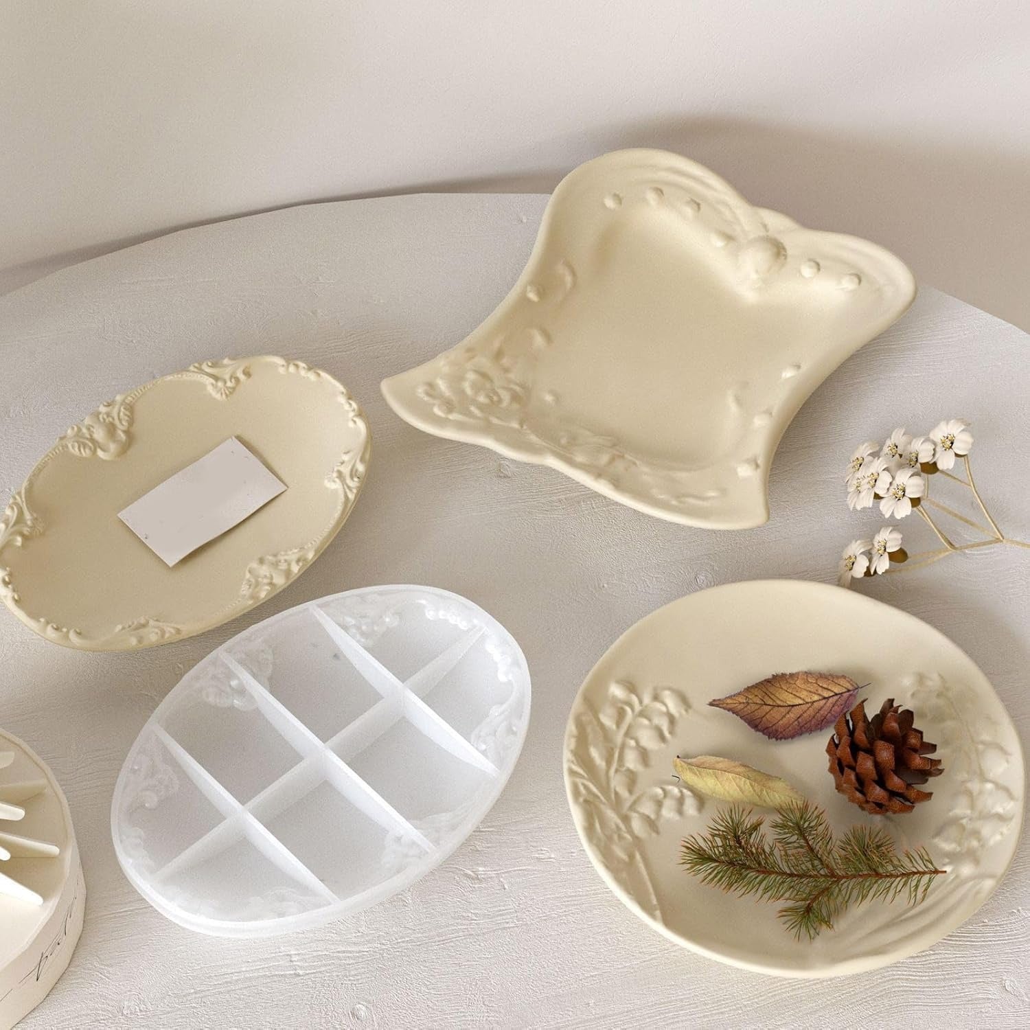 Hand holding finished cream oval vintage floral tray beside butterfly tray and round mould