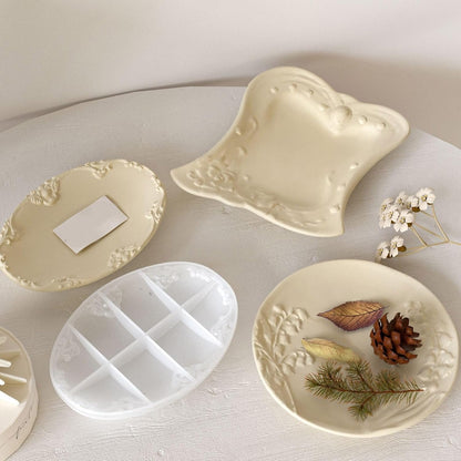 Hand holding finished cream oval vintage floral tray beside butterfly tray and round mould