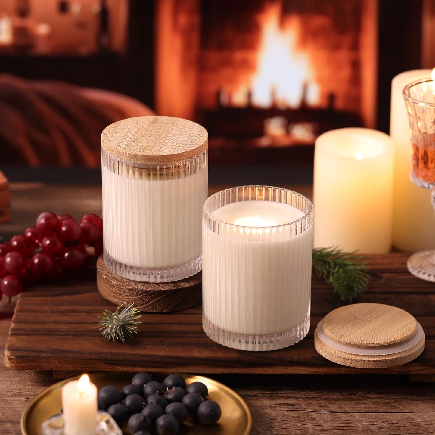 Two ribbed glass candle jars with bamboo lids and lit candles on wooden board by fireplace, cozy winter setting