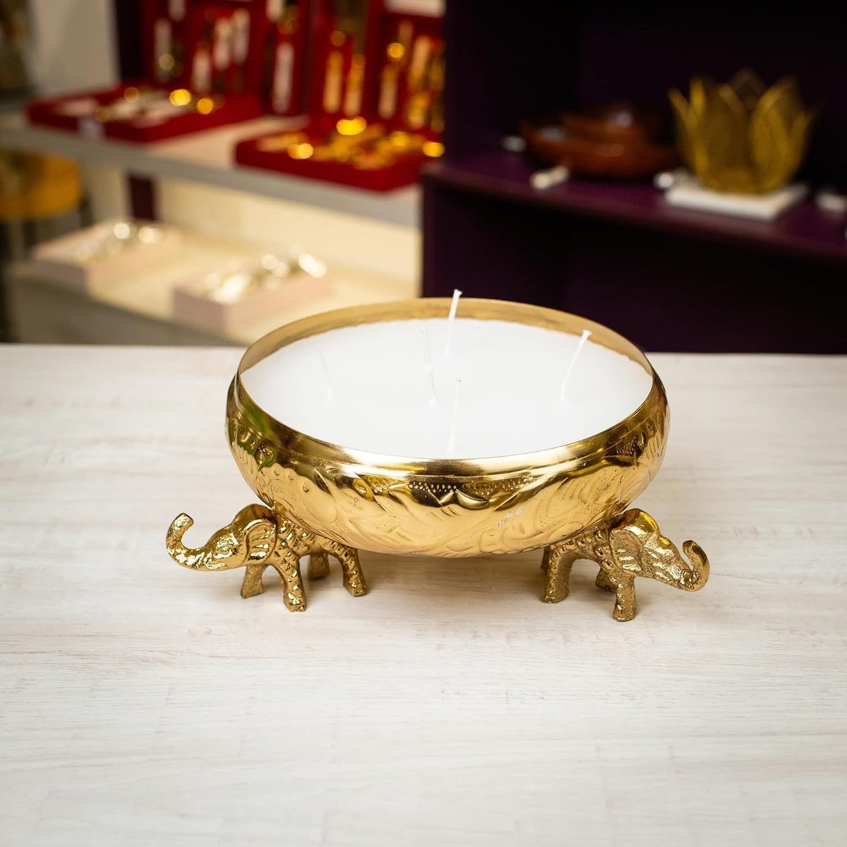 Gold elephant urli candle vessel with multi-wick white candle poured inside, on white background