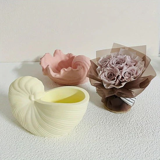 Lifestyle shot of cream nautilus shell bowl candle beside pink ruffled bowl and dried rose bouquet