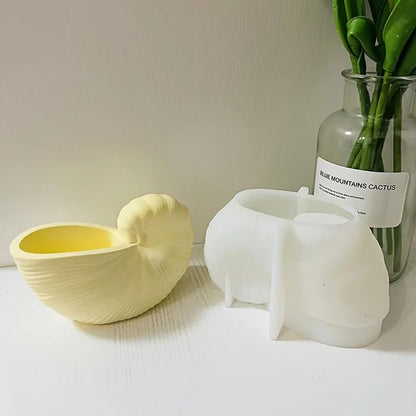 Cream nautilus shell bowl beside white silicone mould and plant on a white surface