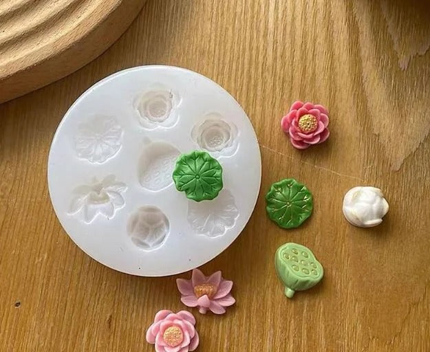 6 cavity lotus flower & leaf silicone mould on wooden surface with finished pieces – pink lotus blooms, green lotus leaf and seed pod in wax or resin