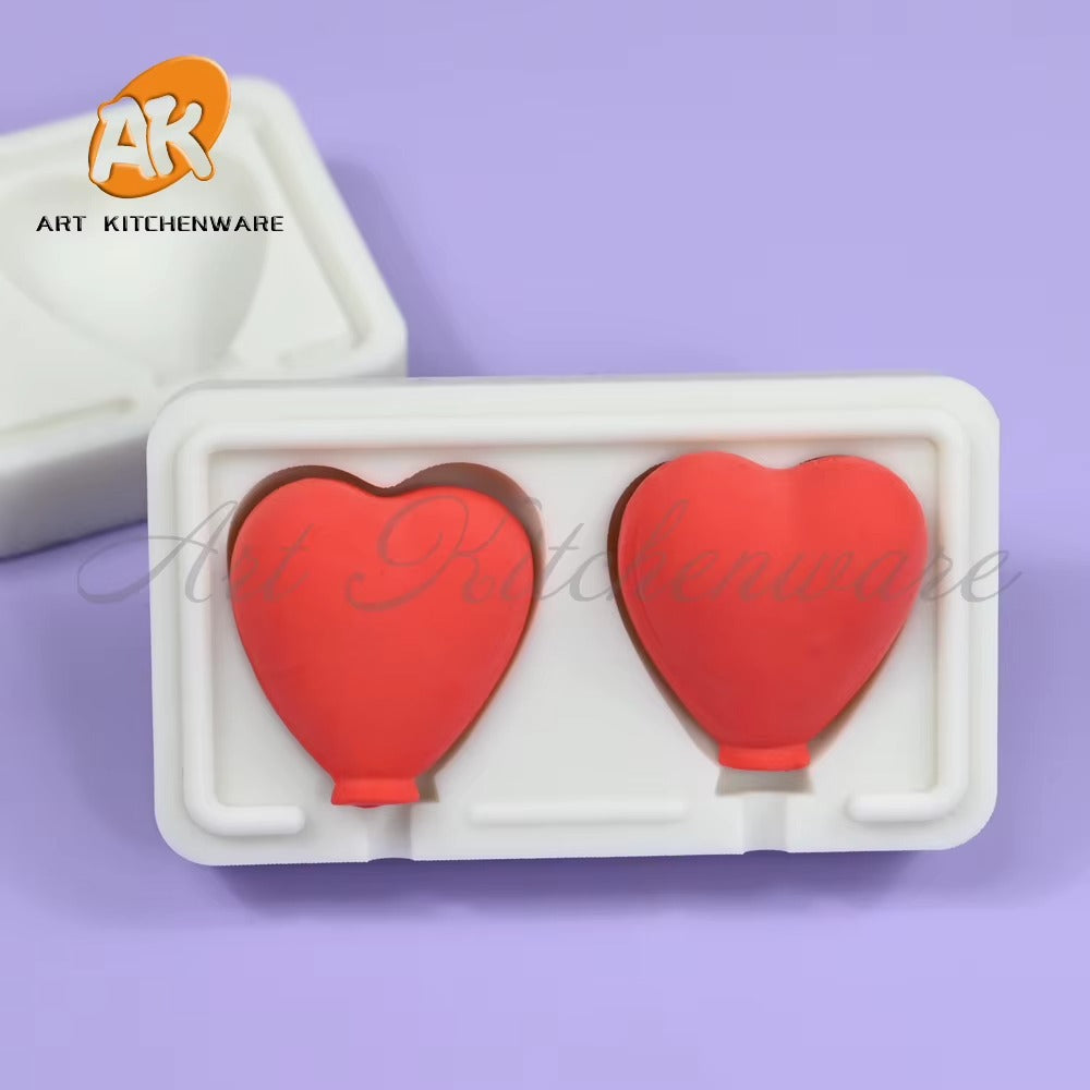 Two red heart sample castings positioned inside a white two-cavity lollipop mould