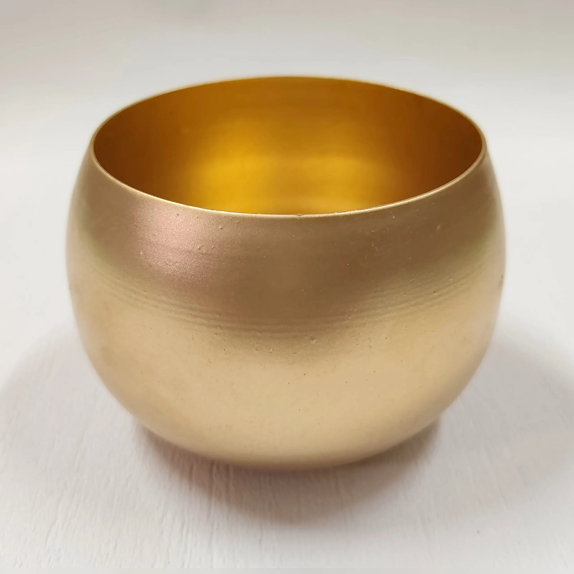 Gold ball candle tin held in hand with green plants in background