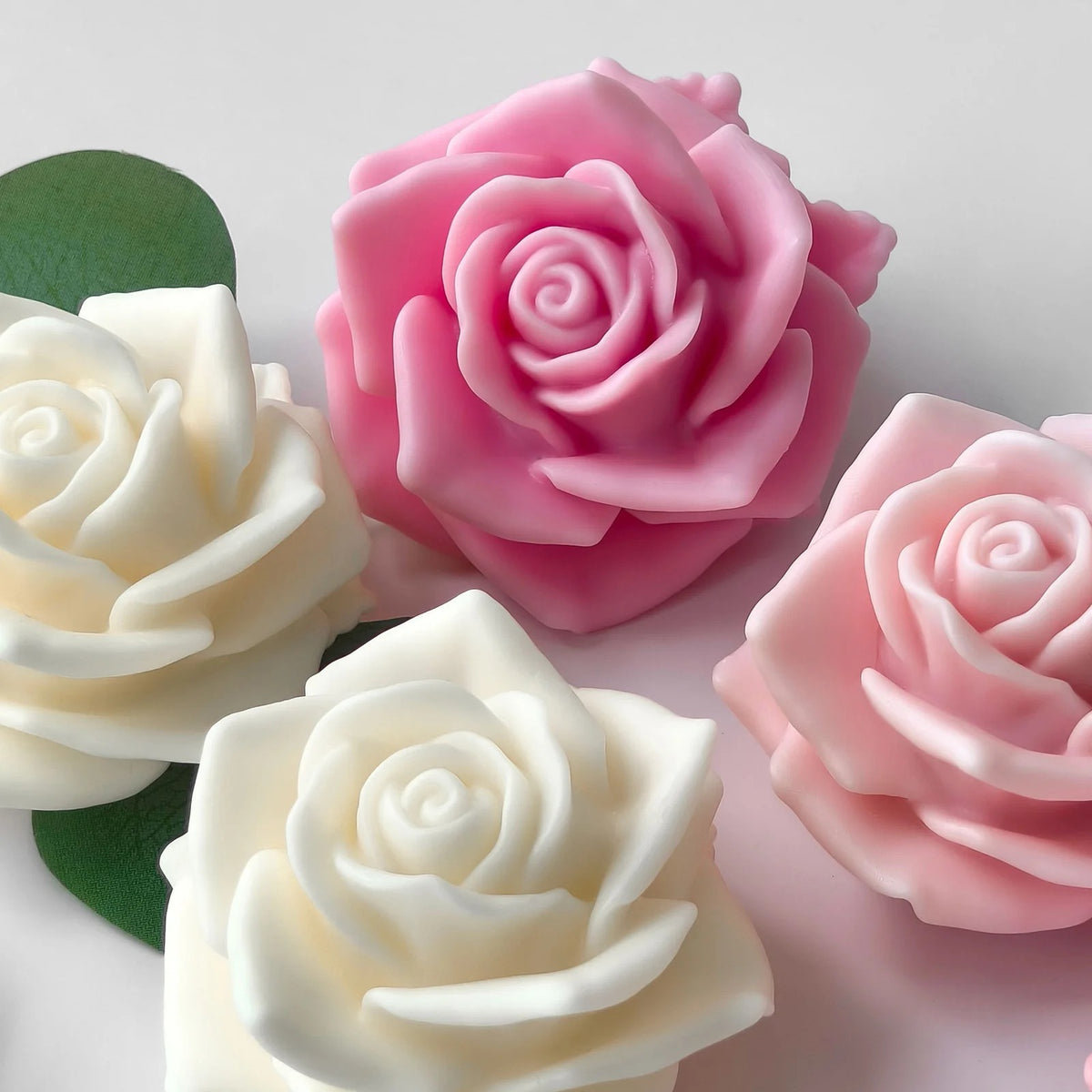 3D full bloom rose silicone candle mould – three finished candles in pink, blush, and ivory on white fabric