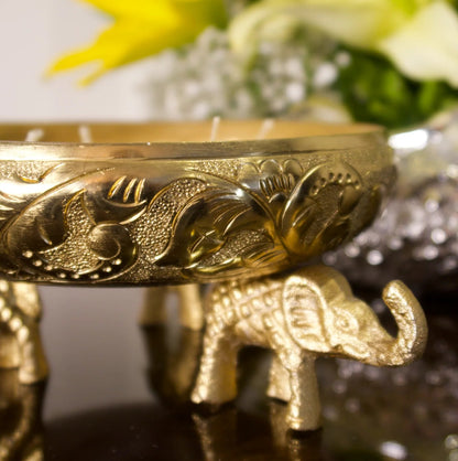Gold elephant urli candle vessel with lit multi-wick candle on bookshelf with books and wicker basket