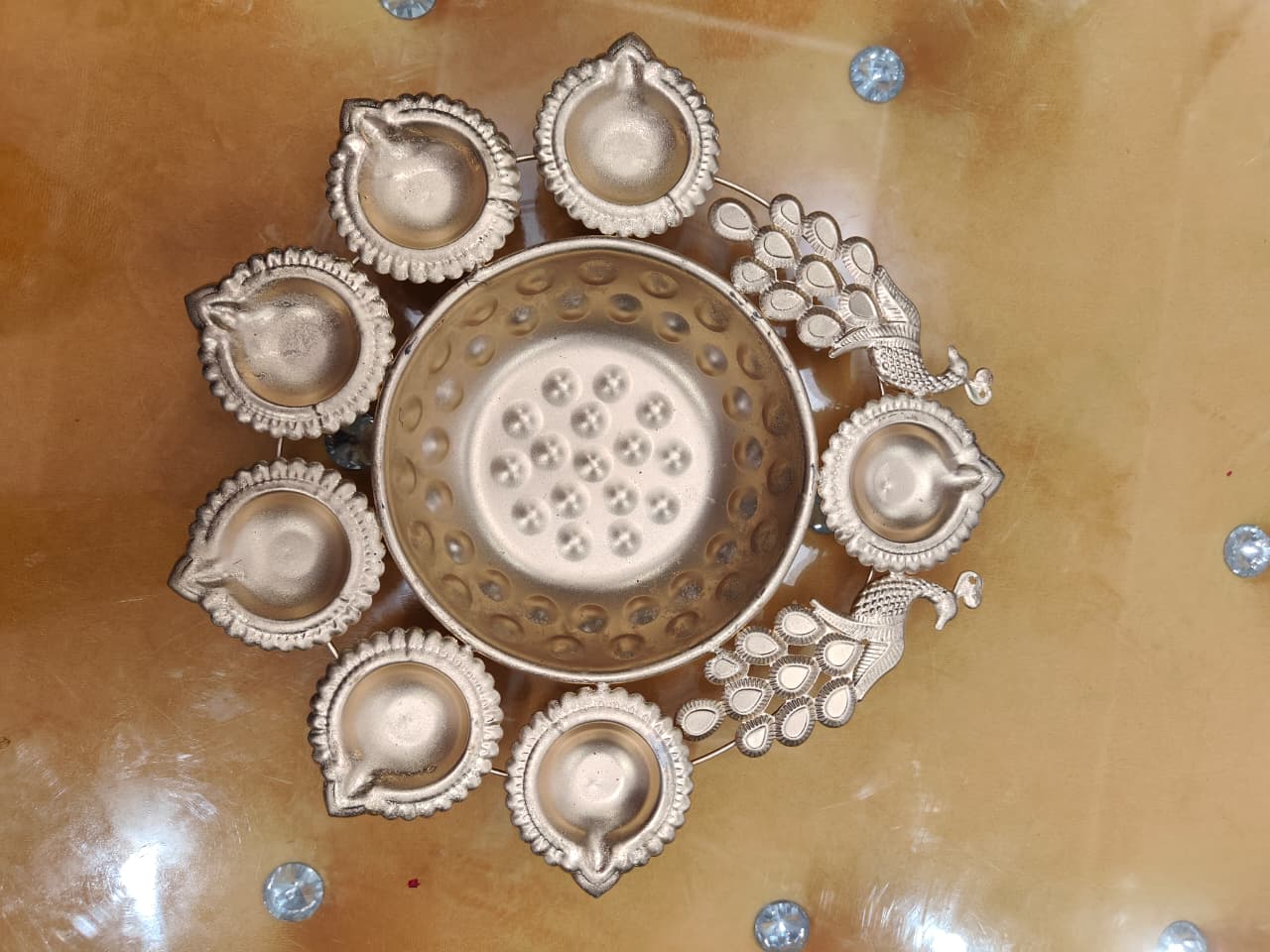 Gold peacock diya urli with 7 scalloped diya holders and 2 peacock figures surrounding central bowl, top view