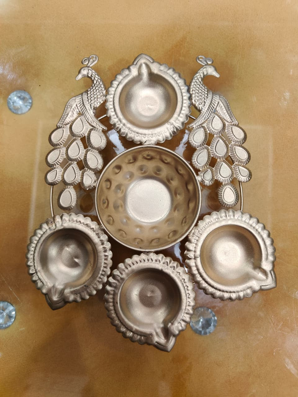 Gold compact twin peacock diya urli with 2 standing peacock figures and 4 scalloped diya holders surrounding central bowl, top view