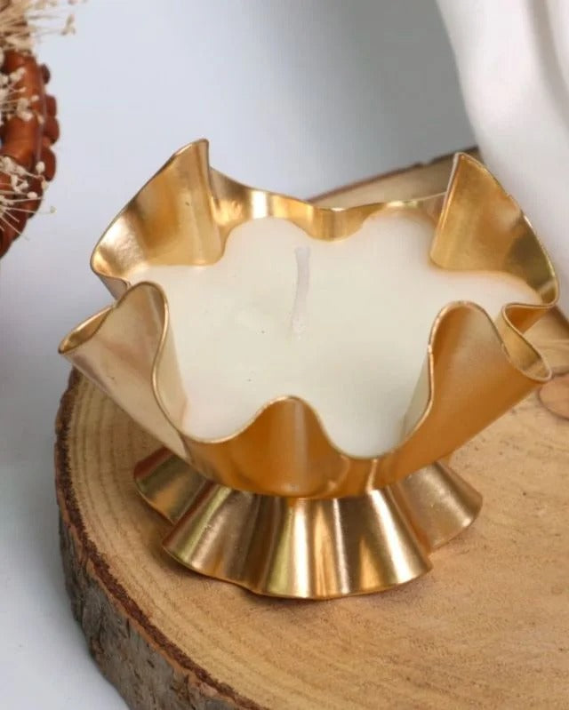 Gold ruffled lotus petal candle vessel with poured white candle on wood slice surface