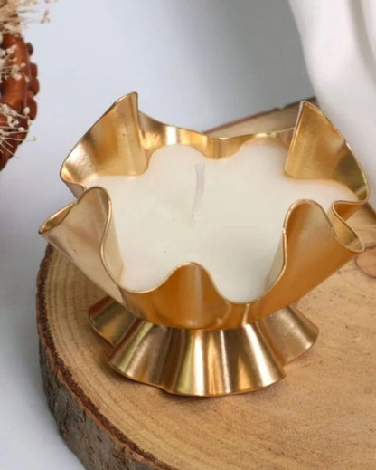 Gold ruffled lotus petal candle vessel with poured white candle on wood slice surface