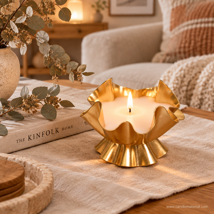 Gold ruffled lotus petal candle vessel with lit candle on cozy living room coffee table with eucalyptus and linen