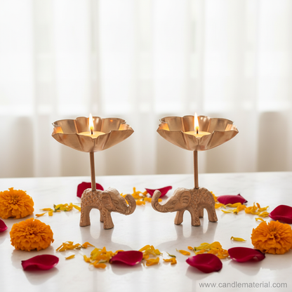 Elephant tall stem lotus diya holders with lit candles on marble surface with marigolds