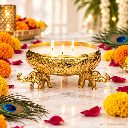 Gold elephant urli candle vessel with lit multi-wick candle on marble surface with marigold flowers and peacock feathers
