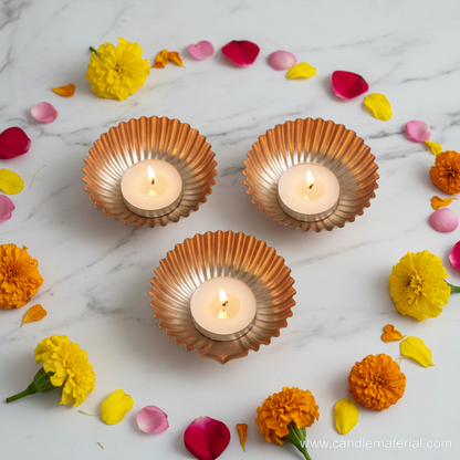 Copper gold diya bowls with lit candles on marble surface with marigolds