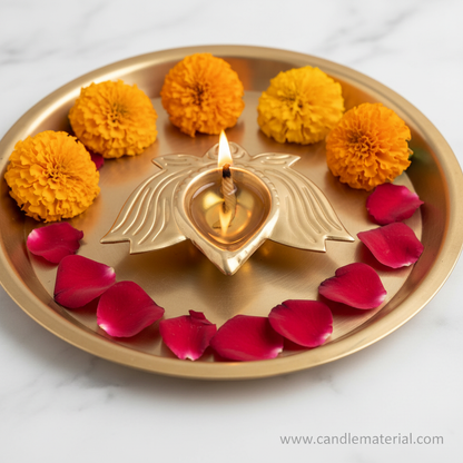 Gold metal lotus diya with lit flame on brass pooja thali with marigold flowers on marble surface