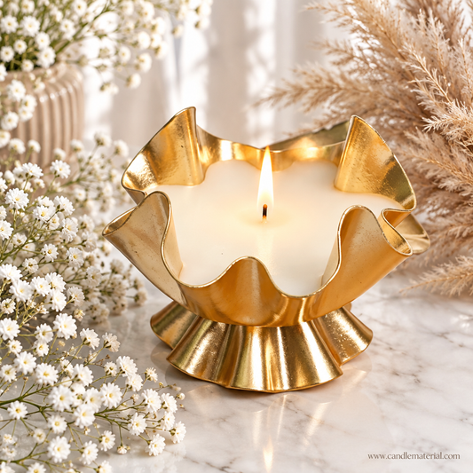 Gold ruffled lotus petal candle vessel with lit white candle on marble surface with baby's breath and pampas grass