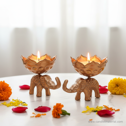 Elephant lotus bud diya holders with lit candles on marble surface with marigolds