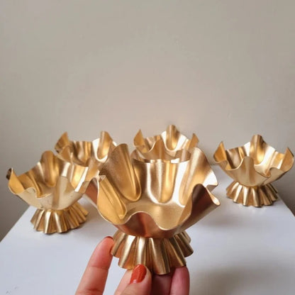 Four gold ruffled lotus petal candle vessels in different sizes grouped together on white surface