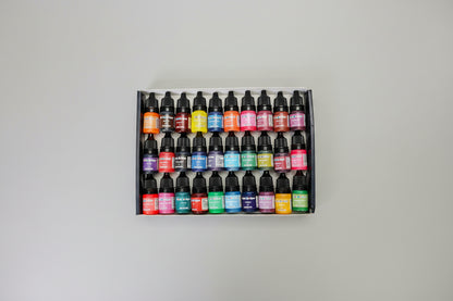 Set of ink bottles in various colors arranged in a box on a dark surface.
